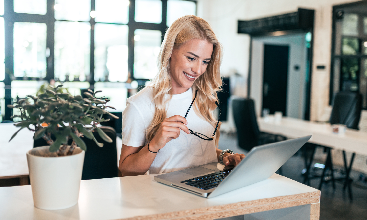 Vrouw met bril in haar hand achter laptop in zakelijke omgeving E-learning